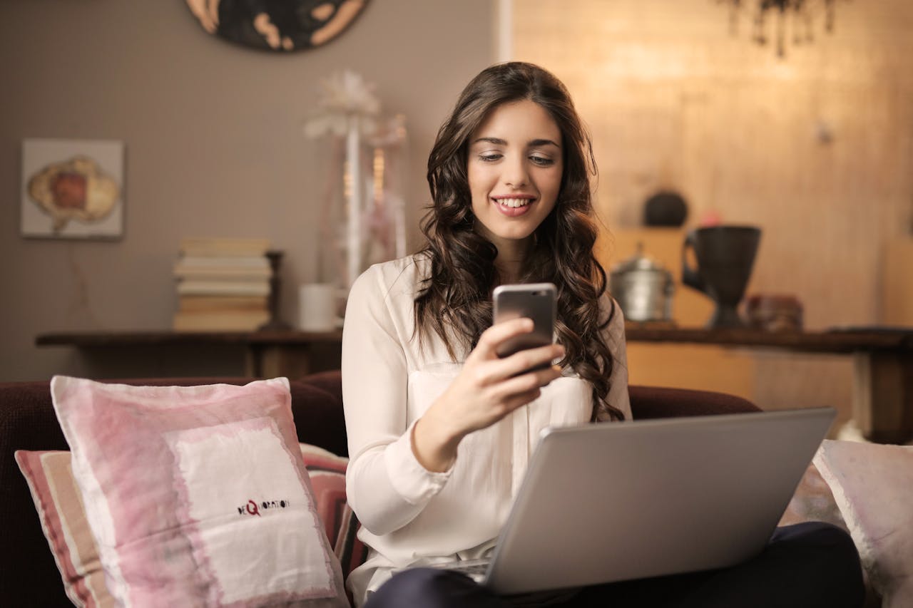 hero-img A woman enjoying leisure time using her smartphone and laptop in a cozy living room.